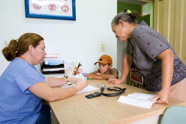 A healthcare worker talks with a woman and child across a desk.